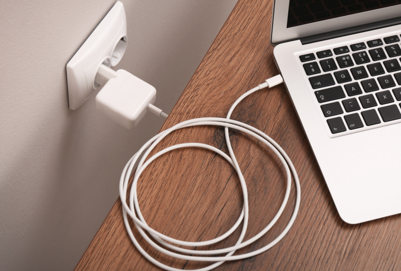 A USB-C laptop charger plugged into a smartphone on a desk