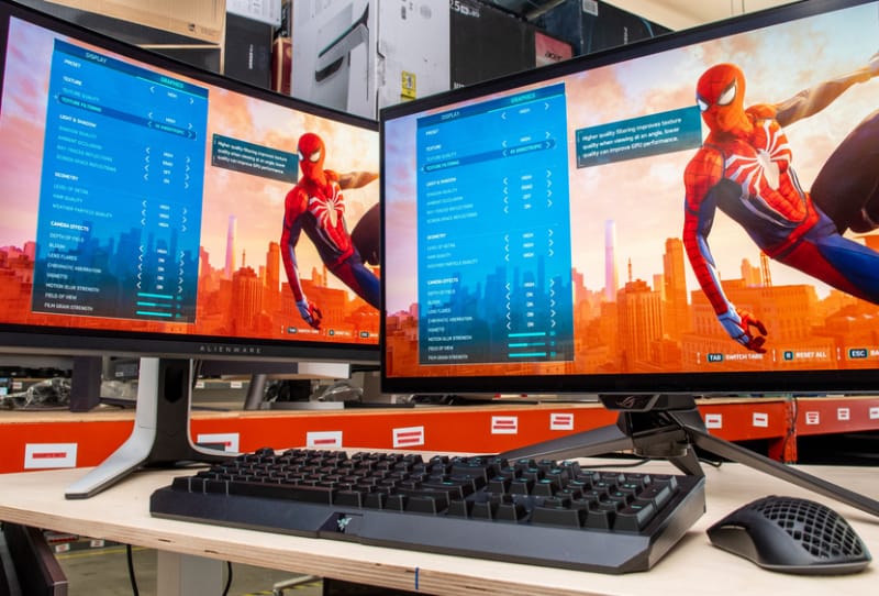 A gaming monitor displaying a first-person shooter on a desk setup with keyboard and mouse
