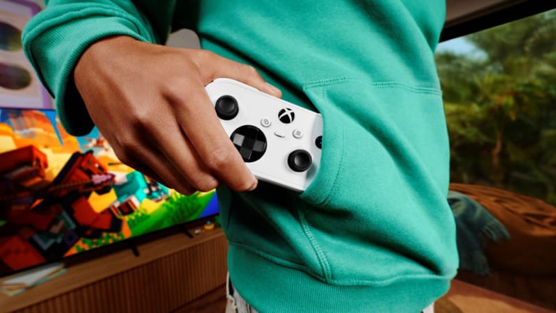 Xbox Nano controller held in one hand next to a smartphone to show its pocket-size footprint